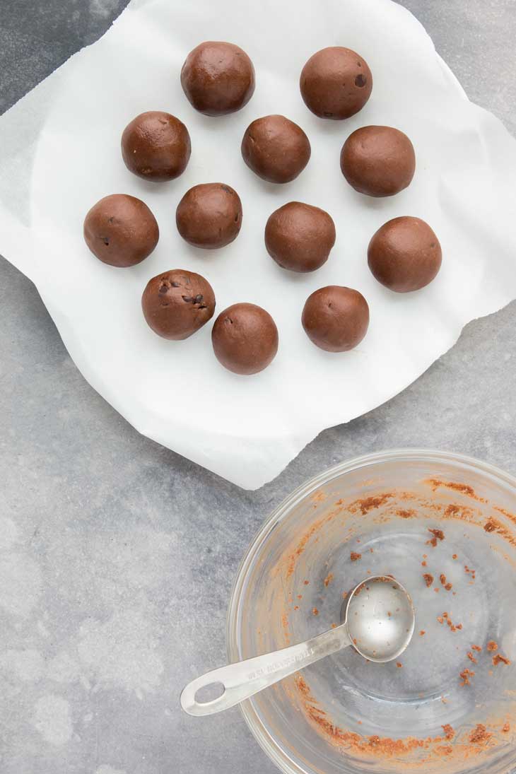 Overhead photograph of chocolate cookie dough bites rolled into balls and sitting on parchment paper. 