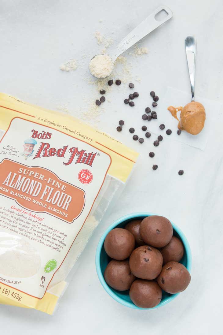 Overhead photograph of chocolate cookie dough bites with peanut butter and bobs red mill almond flour in the background. 