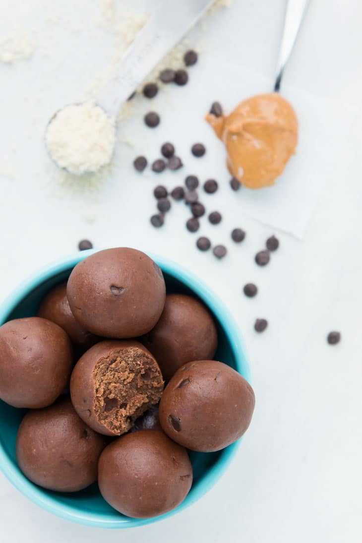 Overhead photograph of chocolate cookie dough bites with peanut butter, almond flour, and chocolate chips in the background.