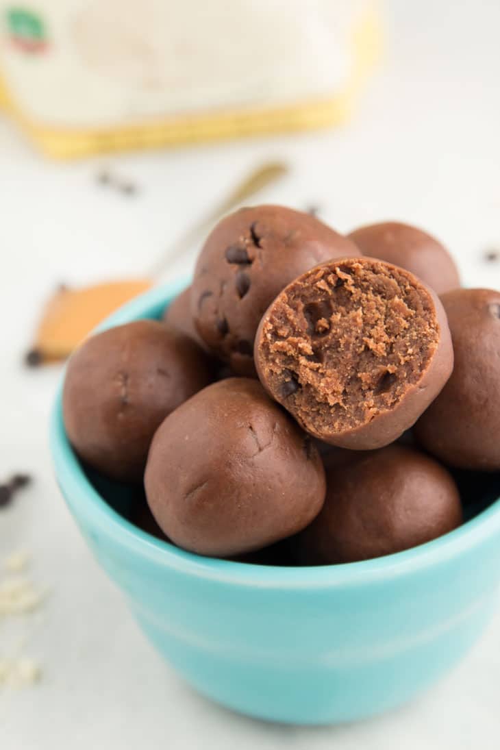 A side closeup photograph of chocolate cookie dough bites. One has a bite taken into it and they are sitting in a blue bowl. 