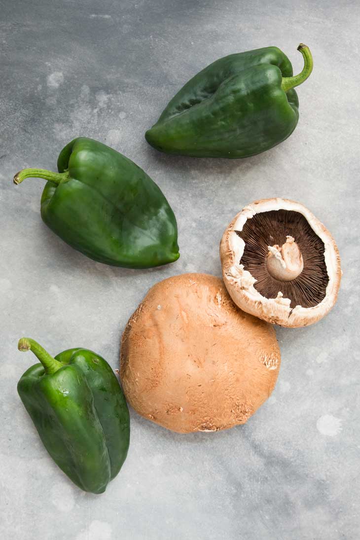 An overhead photograph of whole portobello mushrooms and poblano peppers going into vegan quesadillas.