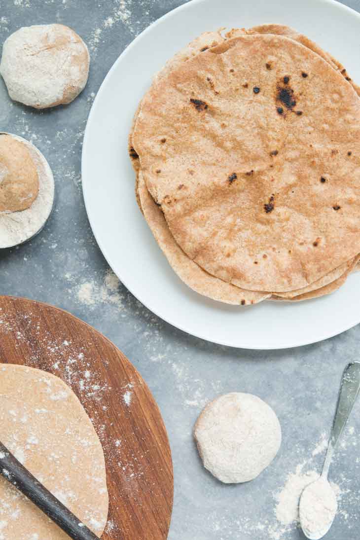 An overhead photograph showing a stack of prepared roti, with flour and dough off to the side.