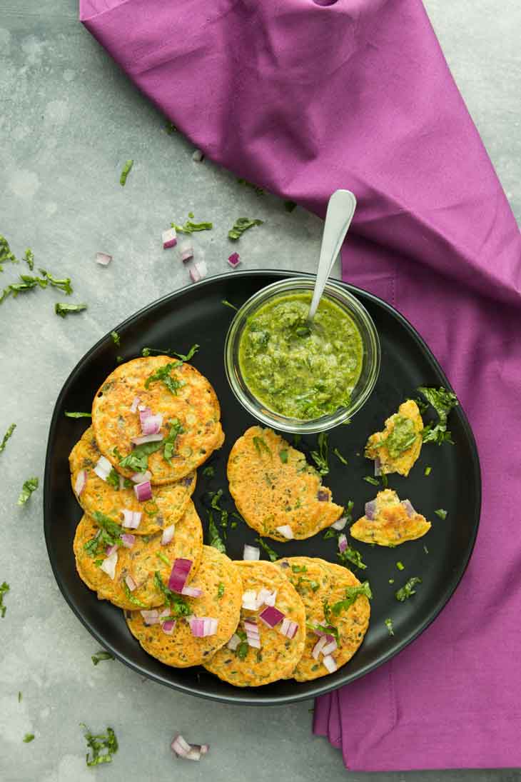 Overhead photograph of vegan vegetable pancakes layered on a black plate with a green sauce.