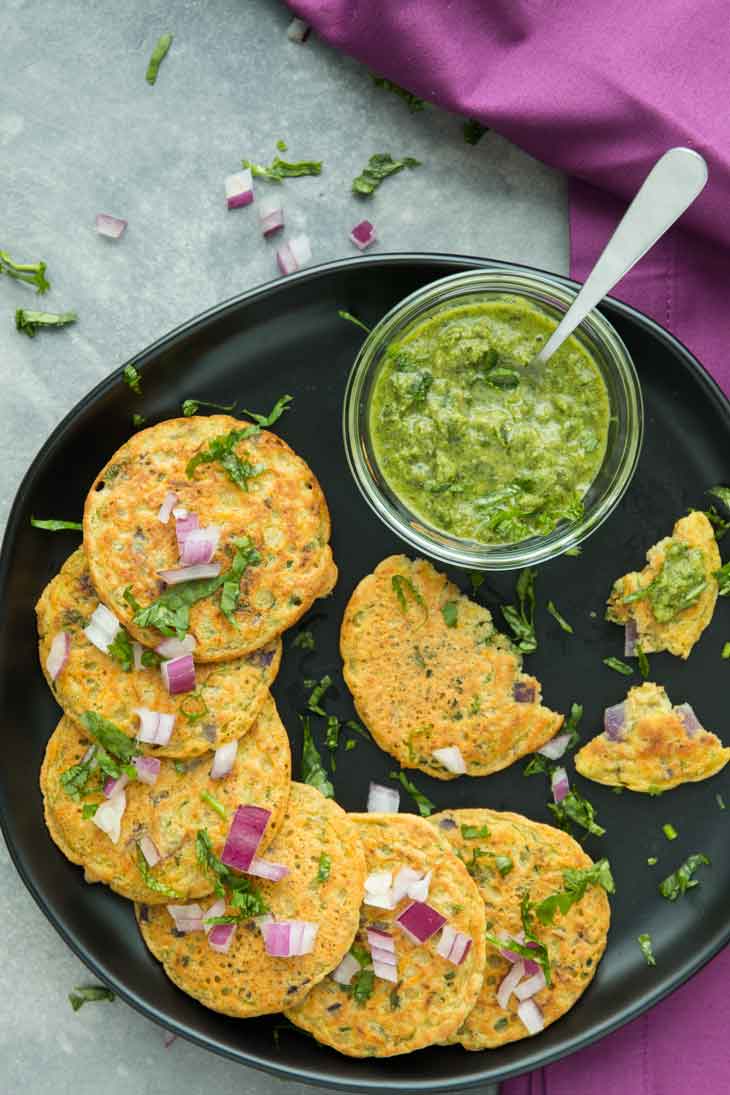 Closeup Overhead photograph of mini savory vegetable pancakes arranged together on a black plate with a green dipping sauce.