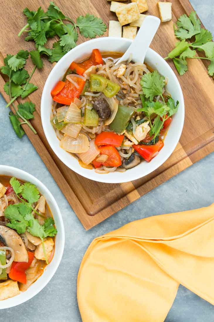 Overhead photograph of two bowls with thai vegan noodle soup, veggies, and tofu. There's cilantro on the side as garnish.