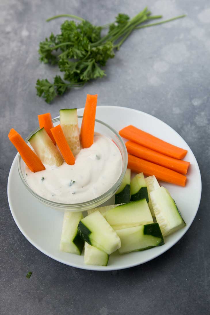 Side photograph of dairy free ranch dressing served with carrots and cucumbers, and parsley on the side. 