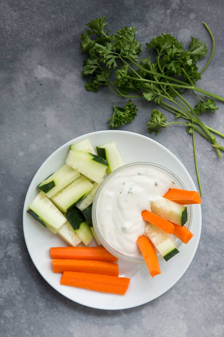 Overhead photograph of vegan dairy free ranch dressing served with carrots and cucumbers.