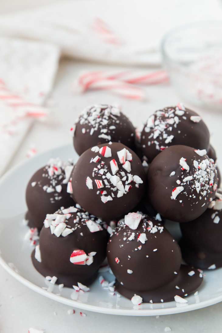 A plate of vegan gluten-free brownie truffles with peppermint and candy canes in the background.