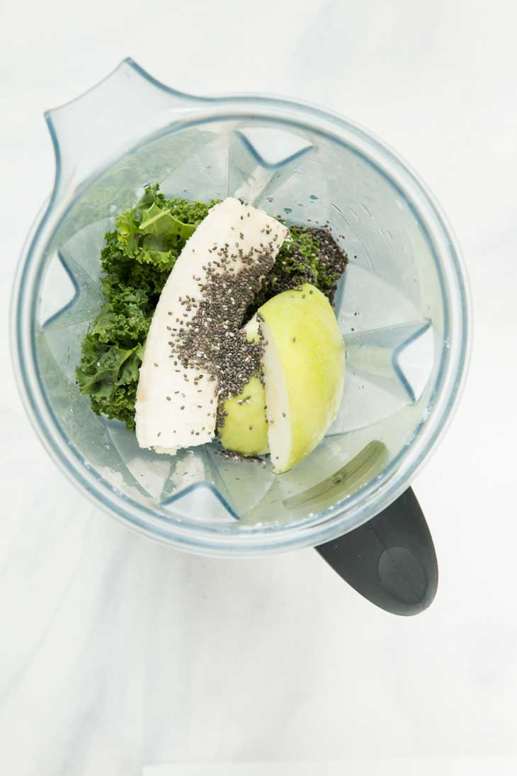 Overhead shot of a vitamix blender containing all the ingredients for a pineapple kale smoothie.