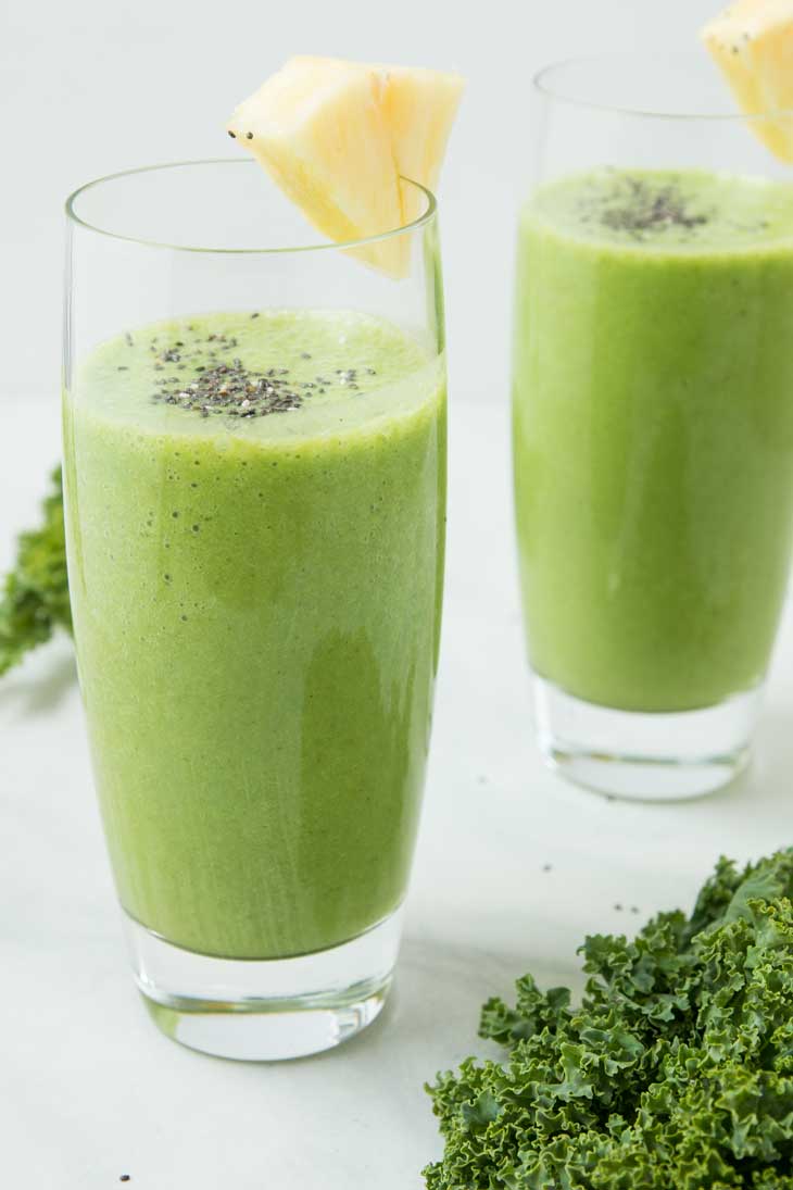 Two tall glasses of pineapple kale smoothie topped with chia seeds and a wedge of pineapple.